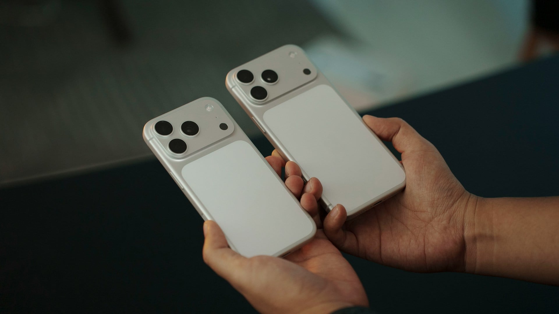 雙手握持兩款全新設計的 Apple iPhone 17 Pro 實機背面,展示銀色機身與獨特的頂部橫向三鏡頭相機模組比較。