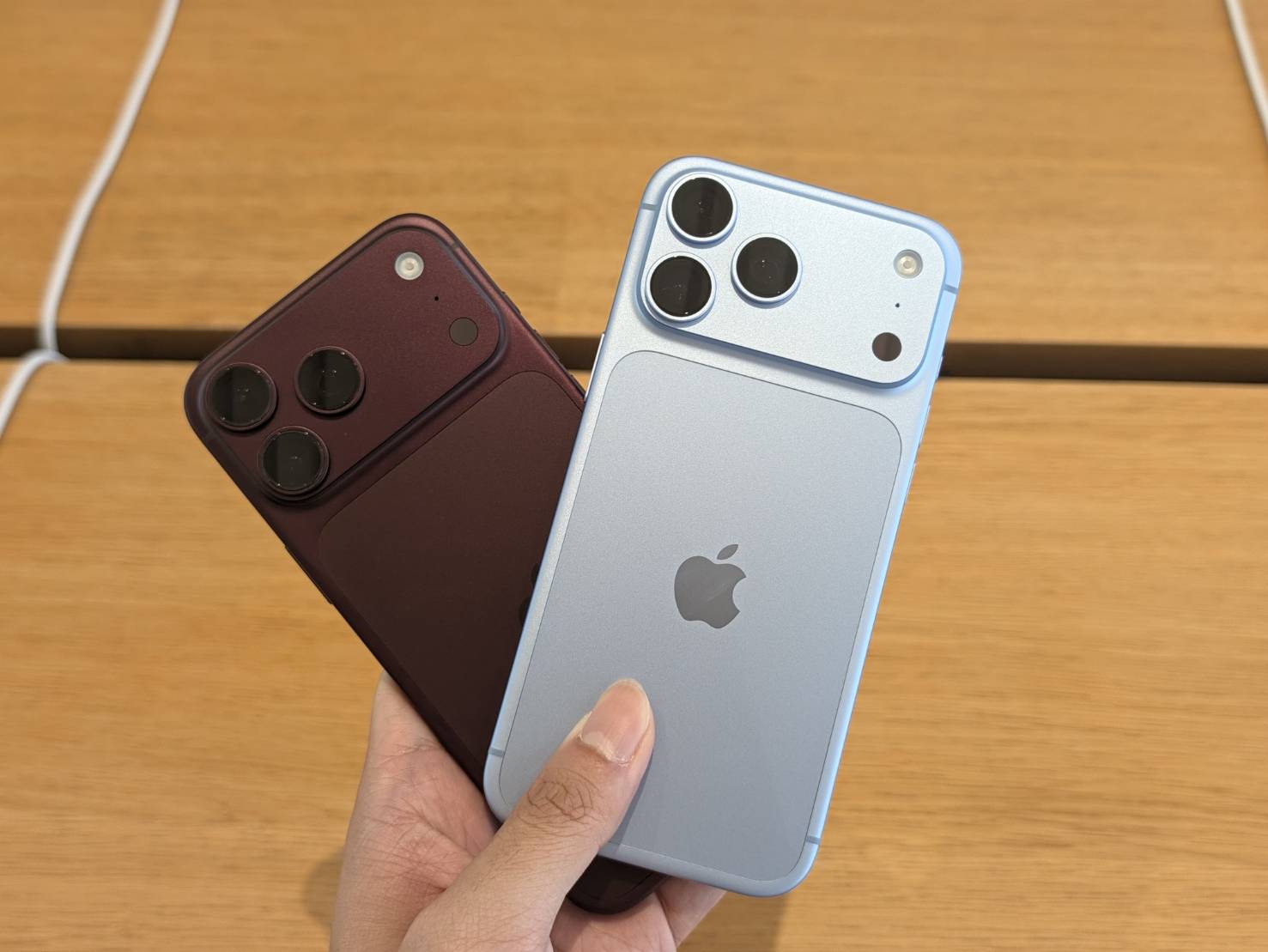 手握淺藍色與深紅色的 iPhone 18 Pro 機身背面,展示三鏡頭模組與 Apple 標誌